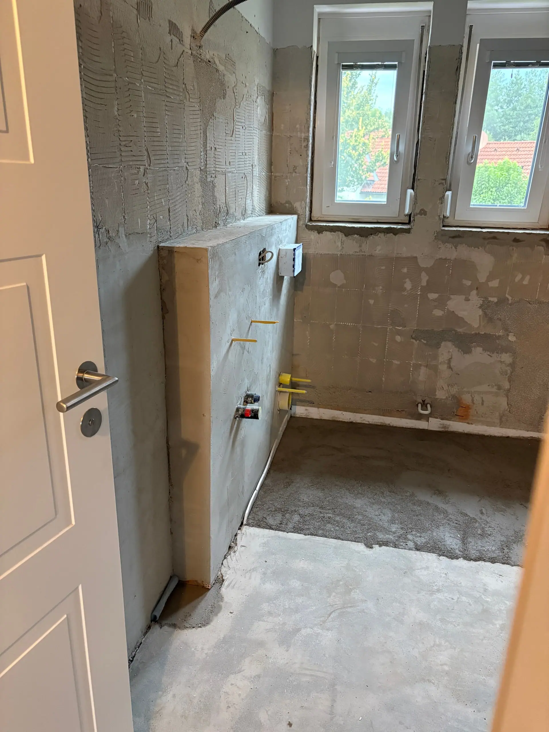 Badezimmer im Umbau: neue Vorwandinstallation mit Anschlüssen, darüber das Fenster, davor der vorbereitete Boden