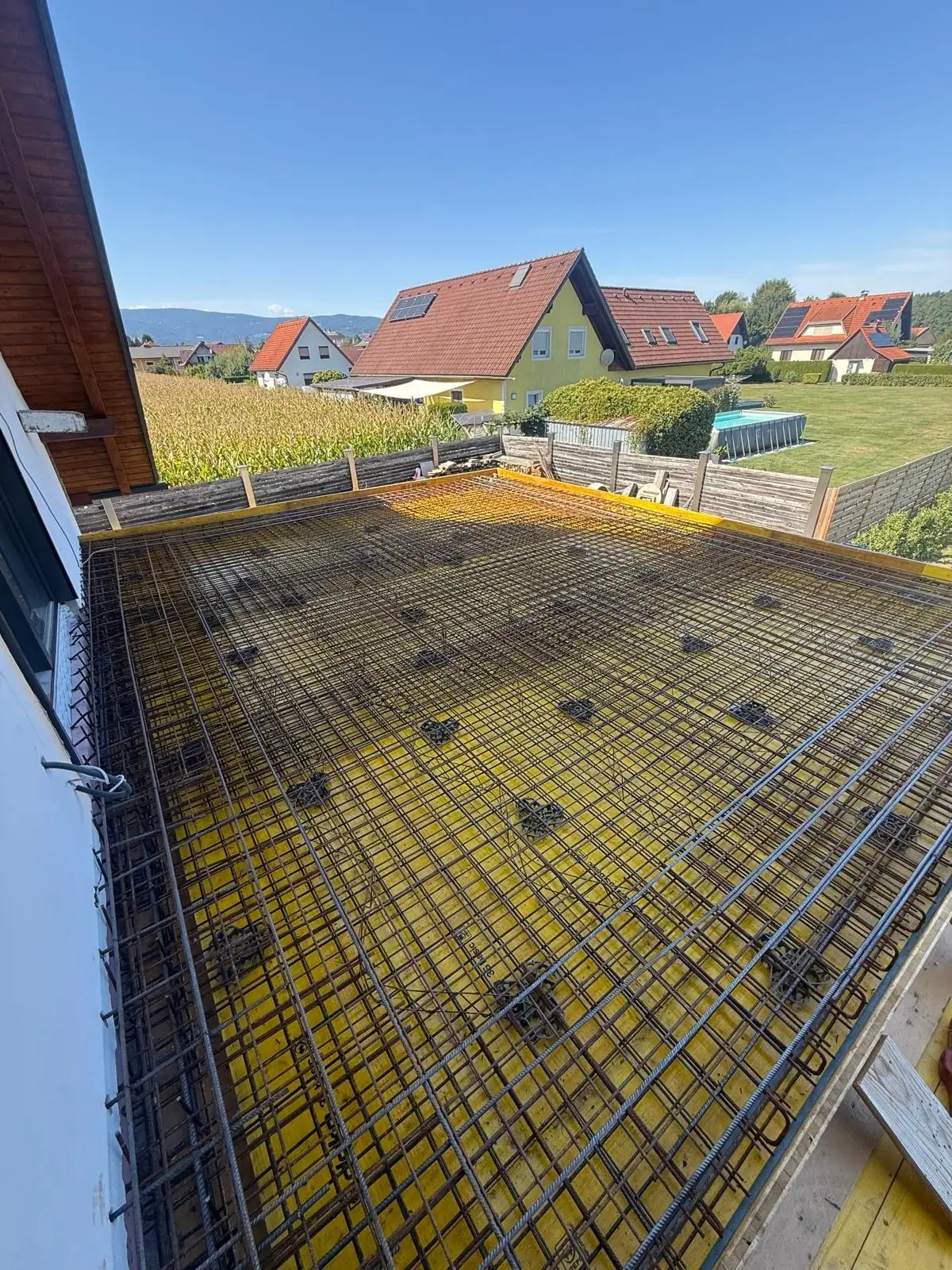 Ecke der Bodenplatte mit Bewehrung neben einer Holzfassade