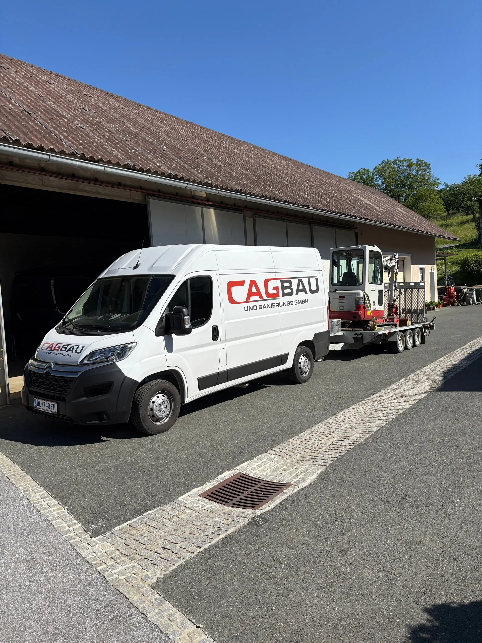 CAG-BAU-Bus mit Anhänger und Minibagger vor einer Halle