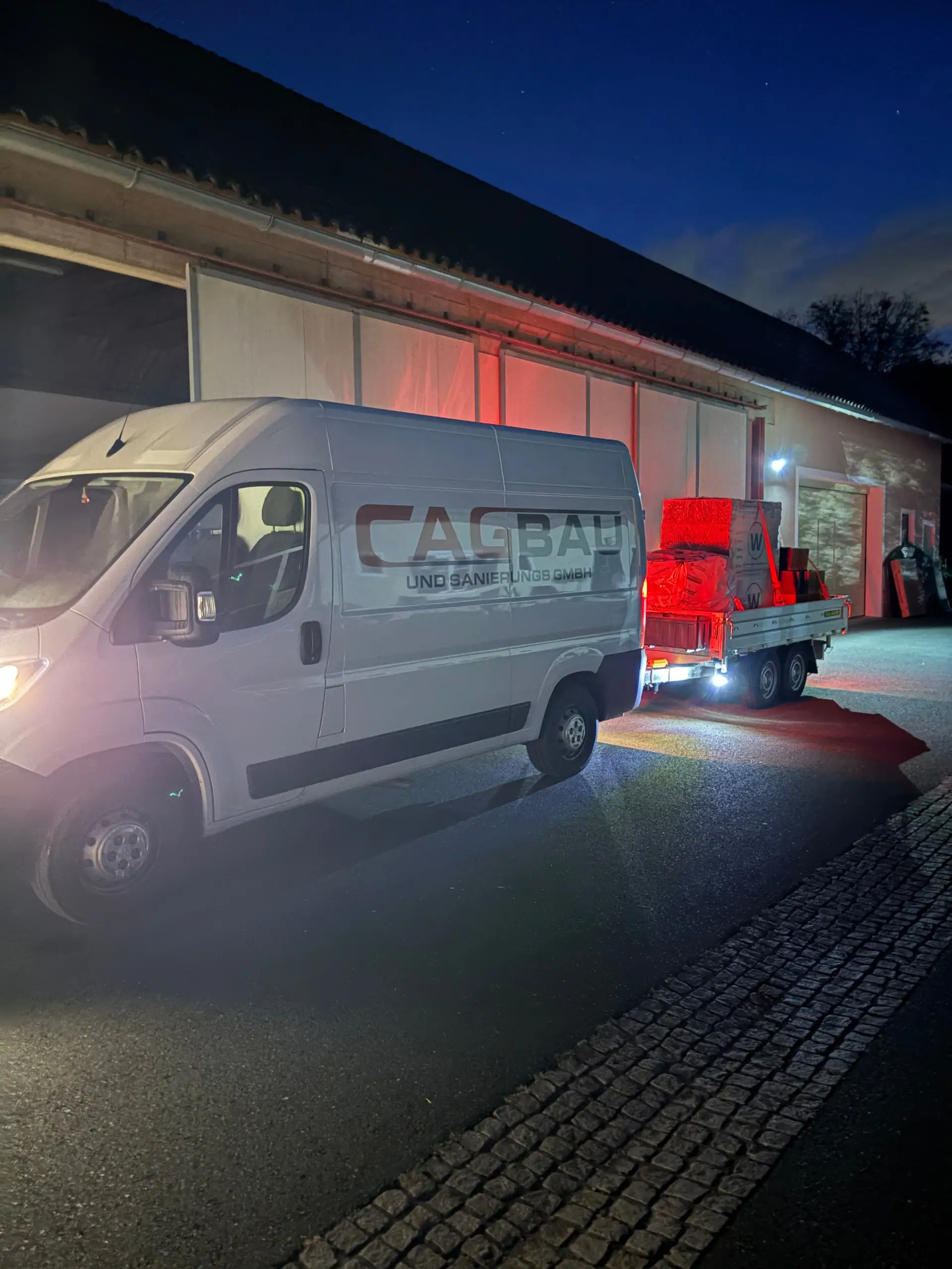 Der Bus von CAG BAU am Abend vor einer beleuchteten Halle