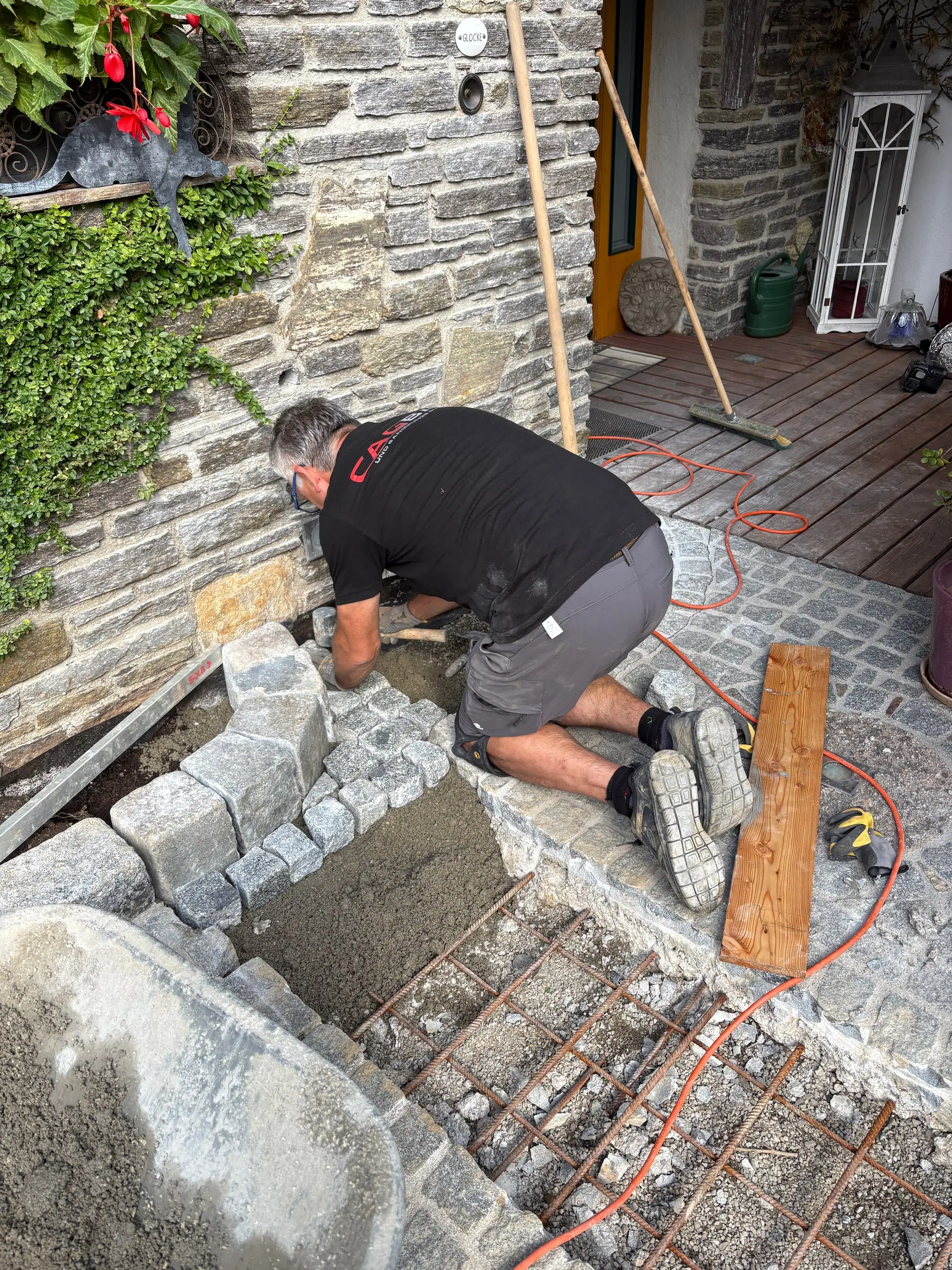 Arbeiter verlegt Kleinsteinpflaster am Hauseingang neben einer Natursteinmauer