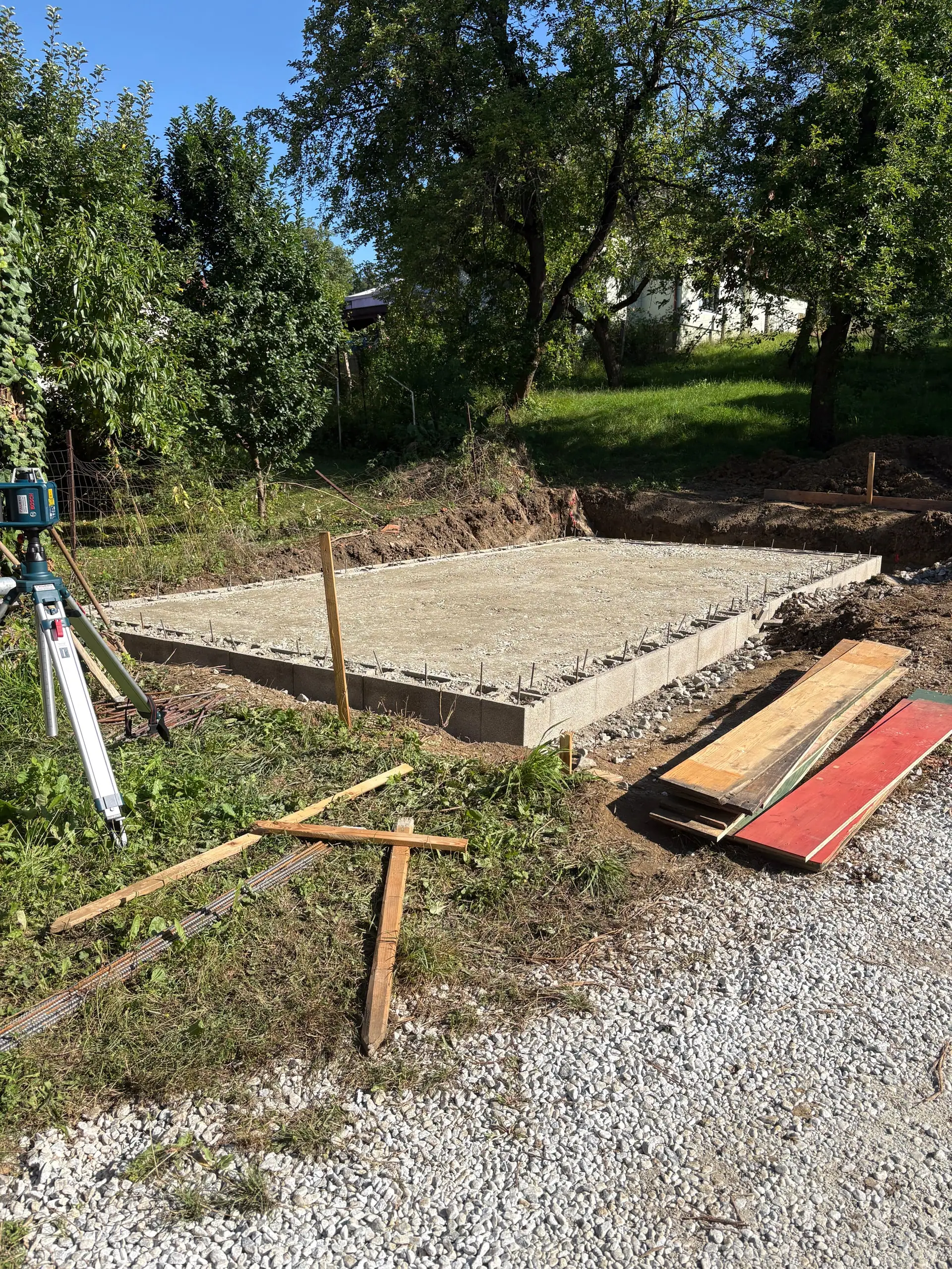 Betonierte Fläche im Garten, daneben Schalbretter und ein Nivelliergerät