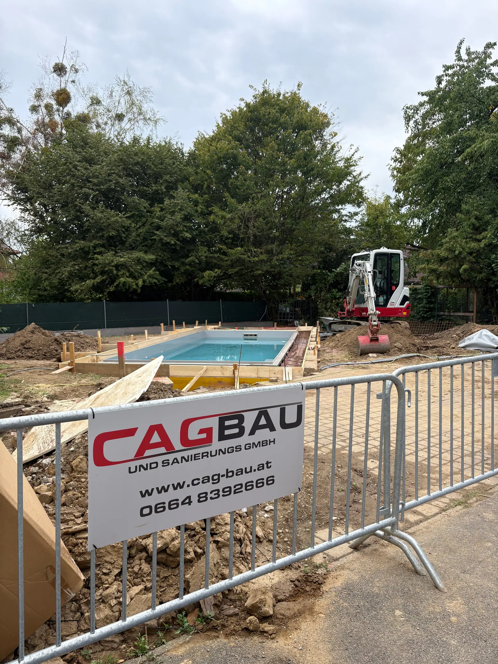 Bauzaun mit CAG-BAU-Banner vor einer Pool-Baustelle