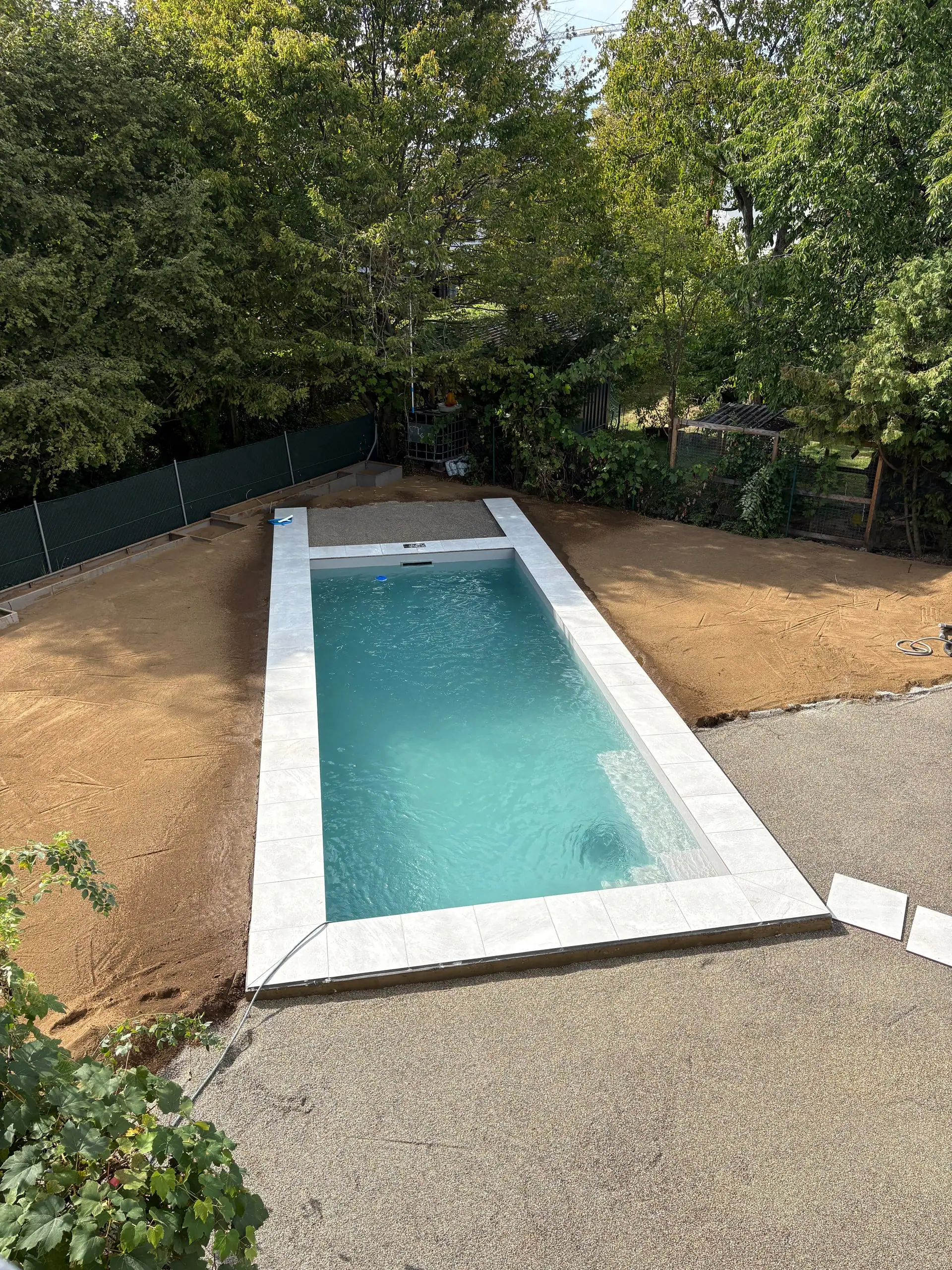 Fertiger Pool mit heller Einfassung in einem Garten, von oben gesehen