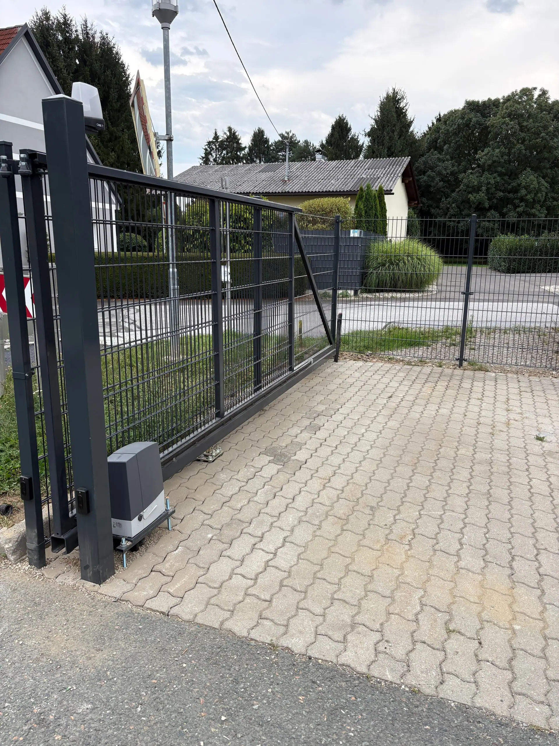 Anthrazitfarbenes Schiebetor mit Antrieb über gepflasterter Einfahrt