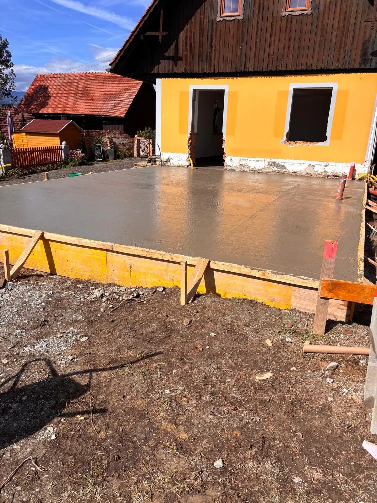 Frisch betonierte, eingeschalte Bodenplatte vor einem gelben Wohnhaus